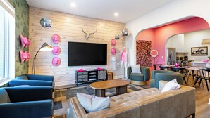 A modern living room with a large flat-screen TV, wooden panel walls, and a mix of seating options including a sofa and armchairs. - Curated Bachelorette Retreat w/ Balcony, Glam Room, Roof | Close to Downtown! (Nashville)