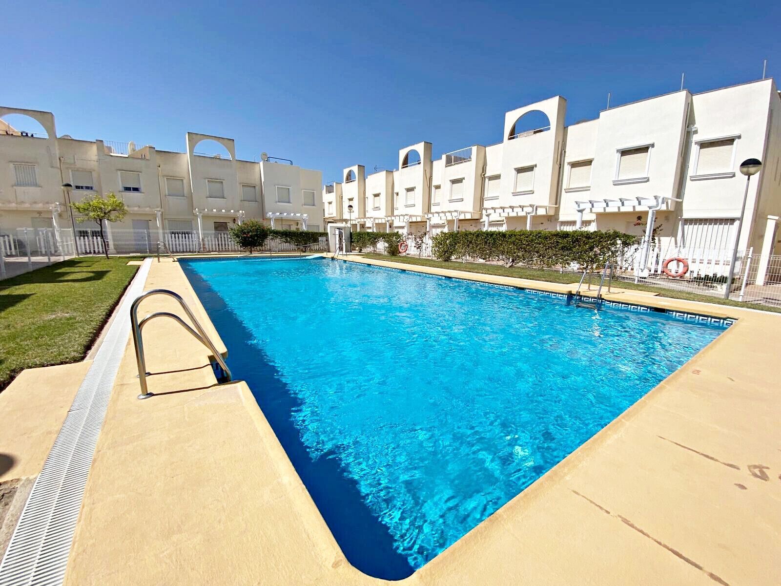 A rectangular swimming pool with clear blue water, surrounded by a beige deck.