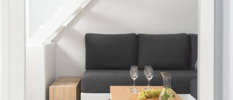 A modern interior with a dark grey sofa, a wooden side table with a glass vase and grapes, and two wine glasses.