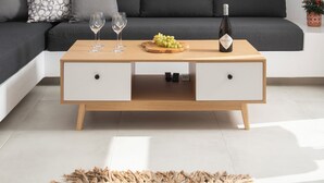 Una sala moderna con un sofá gris, una mesa de centro de madera con copas de vino y uvas, y una pequeña planta en maceta.