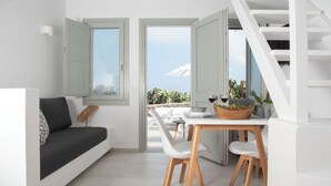 Una sala de estar moderna con sofá, mesa de comedor y sillas. Ventanas abiertas con vistas a zonas verdes y cielo despejado.