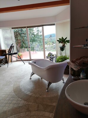 Relax in a spacious room with a bathtub and sliding glass door leading to a patio overlooking a lush garden.
