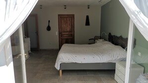 A bedroom with a bed, a wooden door, a headboard, a nightstand, and a window with curtains.