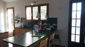 A kitchen with a large island, wooden cabinets, and a window with a view of greenery. There are two yellow chairs at the island and a sink with a faucet.