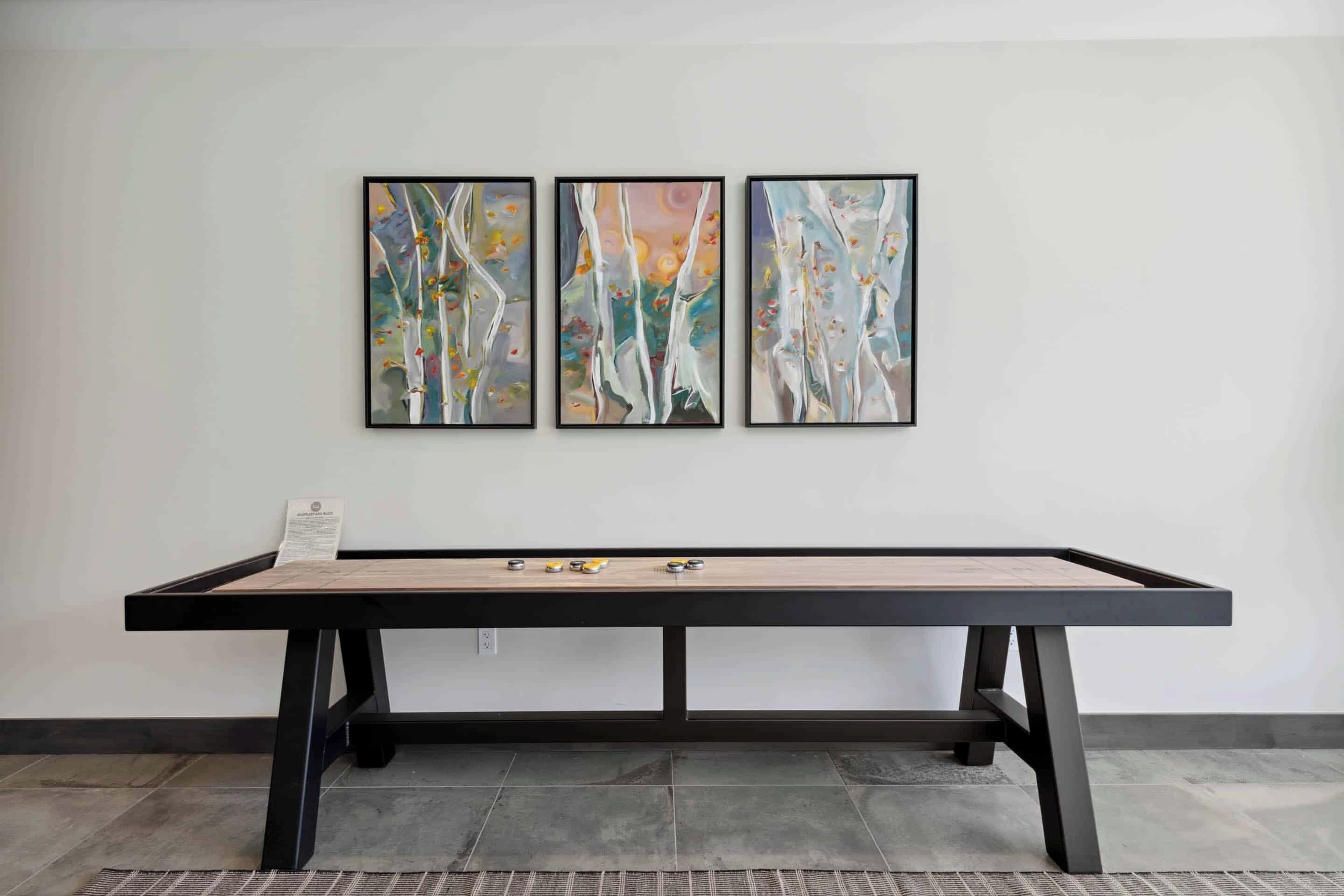 Une pièce avec une longue table, trois tableaux abstraits encadrés accrochés au mur et un petit morceau de papier posé sur la table.