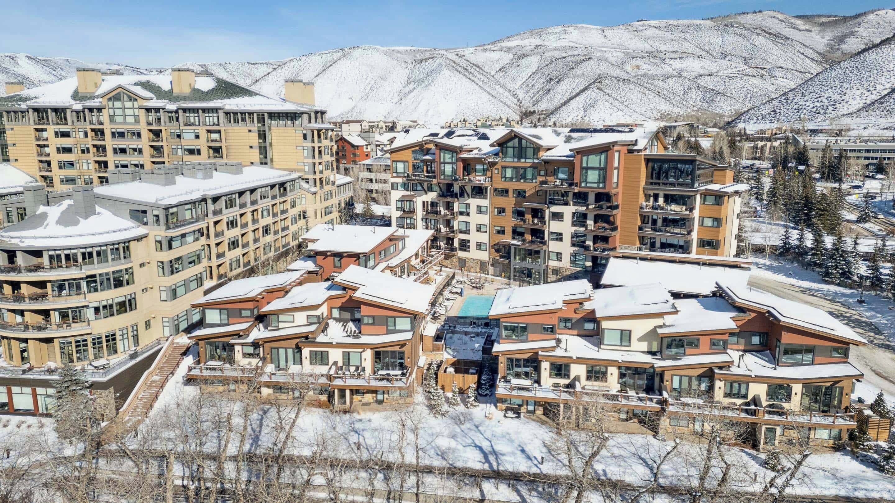 Un complejo turístico nevado con edificios modernos, piscina y vistas a las montañas.