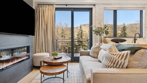 Un salon moderne doté d’une cheminée, d’un canapé, d’une table basse et offrant une vue sur un paysage montagneux grâce à de grandes fenêtres.