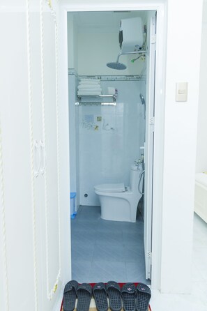 A bathroom with a shower, toilet, and a pair of slippers on the floor. -  Ruby Hotel Phan Thiet (Tien Thanh)