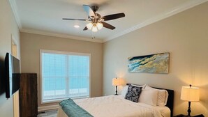 A bedroom with a bed, two bedside lamps, a ceiling fan, a window with blinds, and a painting on the wall.