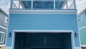 A two-story building with a large garage entrance, a balcony on the upper floor, and a clear sky in the background.