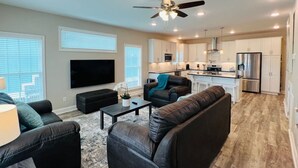 A modern living room with a flat-screen TV, leather sofas, a coffee table, and a ceiling fan.