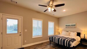 Une chambre à coucher avec un lit, deux lampes de chevet, un ventilateur de plafond et une porte avec une fenêtre.