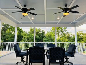 Une terrasse extérieure couverte, dotée d’une table et de chaises, de ventilateurs de plafond et d’une rambarde blanche.