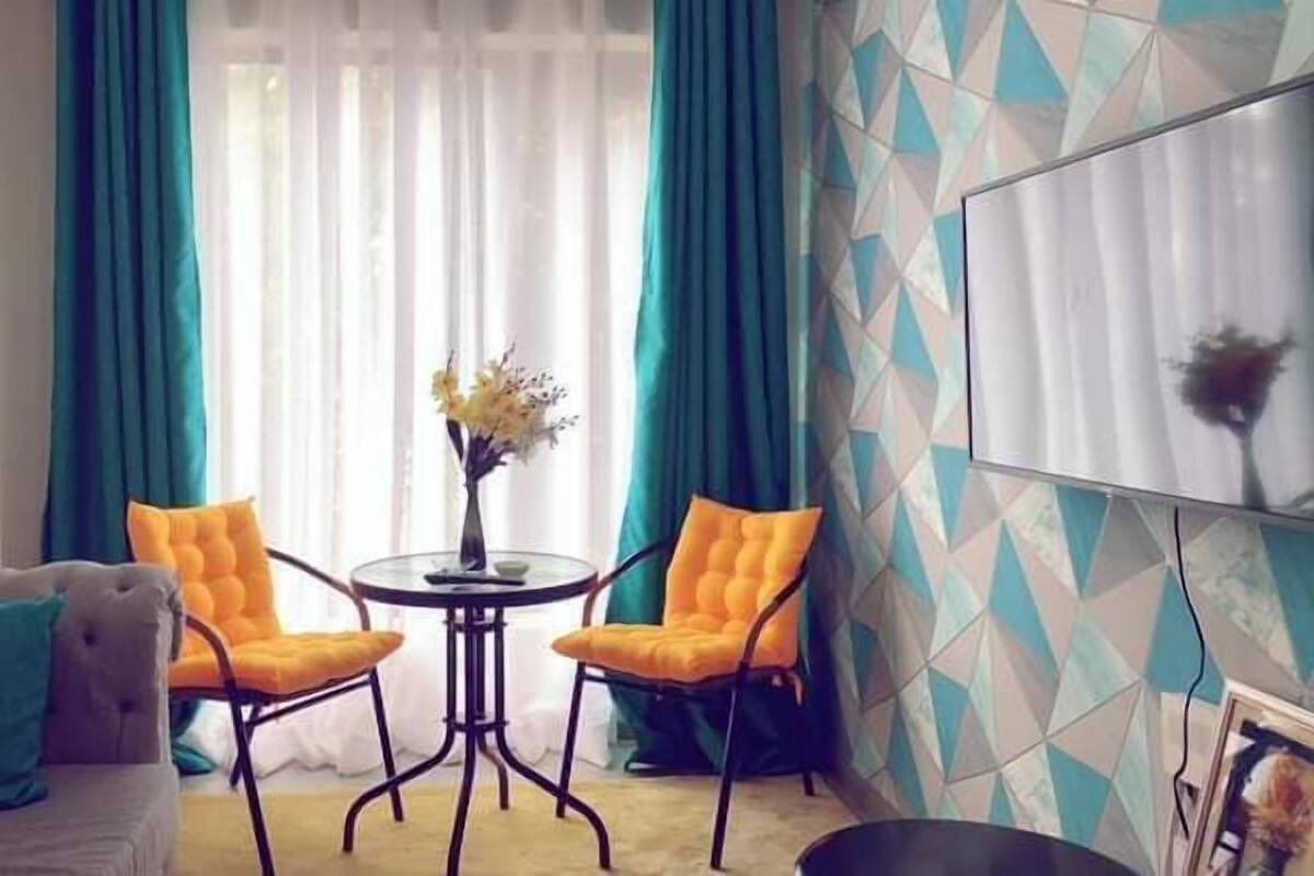 Een kamer met een bank, twee stoelen, een kleine ronde tafel met een bloevas, en een wand met een geometrisch patroon.
