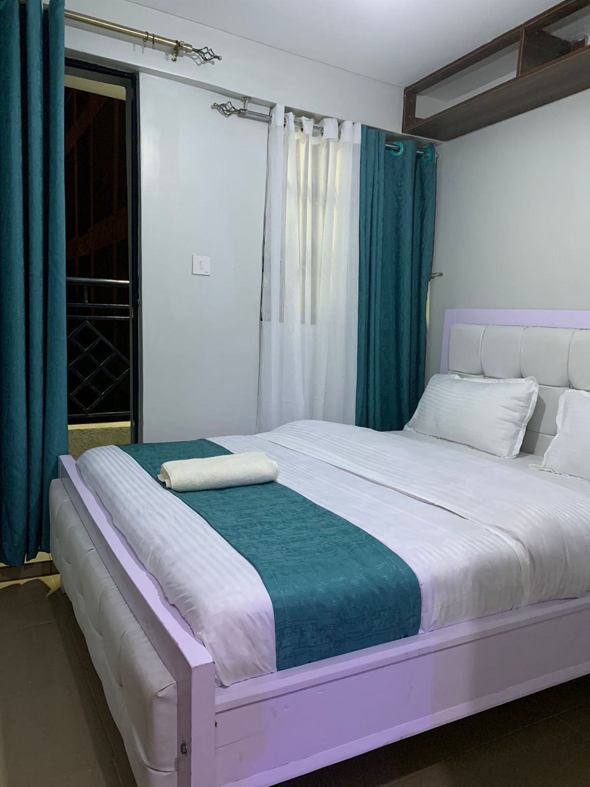 A neatly made bed with white and teal bedding, a teal throw blanket, and a white pillow.