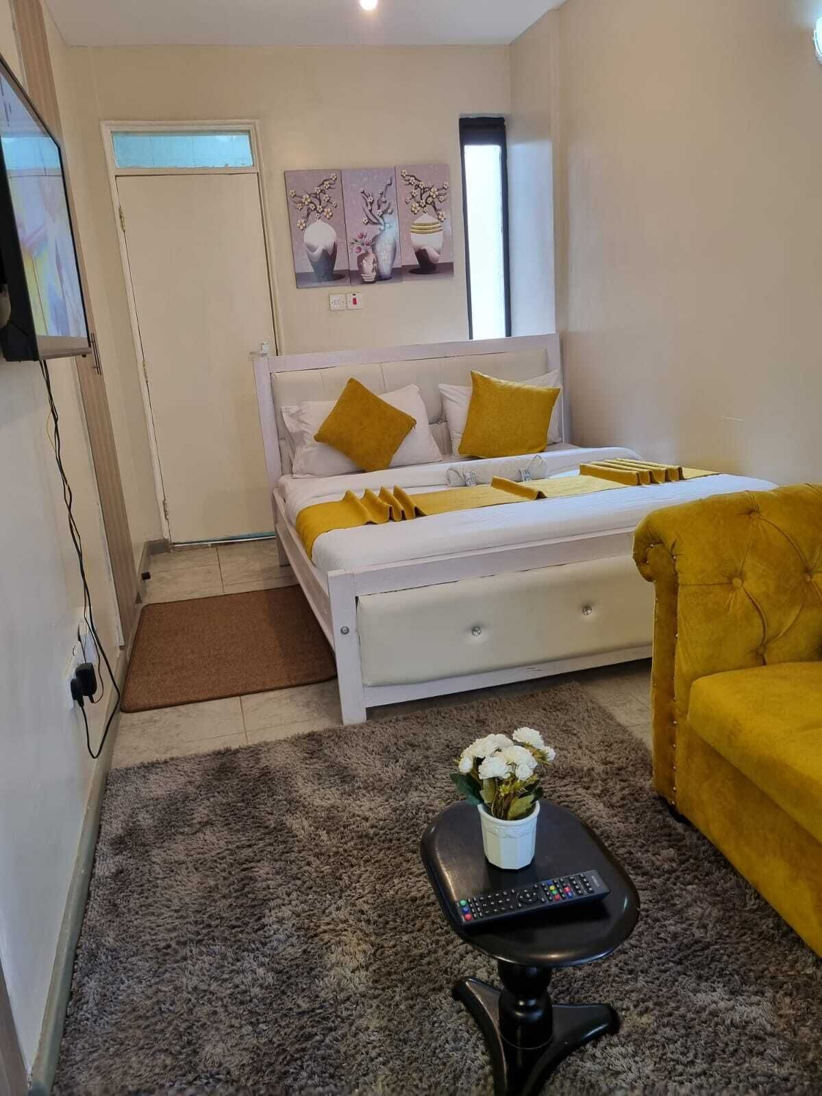 A bedroom with a bed, a sofa, a small table with a vase, and a painting on the wall.