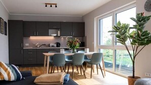 Une cuisine moderne avec des meubles de couleur sombre, un coin repas comprenant une table et des chaises, et une grande fenêtre donnant sur un paysage verdoyant.