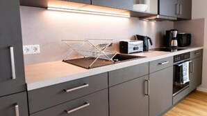 A modern kitchen with grey cabinets, a stainless steel range hood, a coffee maker, and a microwave. - Moderne & Familienfreundliche Ferienwohnung am Goitzschesee (Muldestausee)