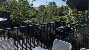 An outdoor patio with a table and chairs, a grill, and a view of trees and a lake. - Moderne & Familienfreundliche Ferienwohnung am Goitzschesee (Muldestausee)