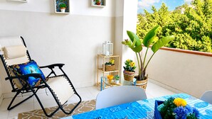 A balcony with a chair, a table with a blue tablecloth, and potted plants. - Appartamenti Abate Riva del Golfo Home (Alcamo)