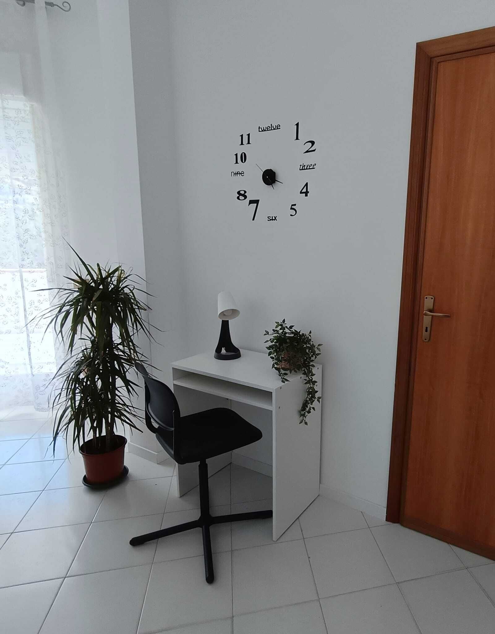 Un bureau blanc avec une chaise noire, une horloge murale, une plante en pot et une porte.