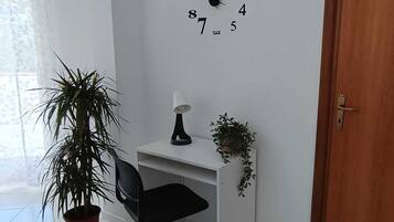 Un bureau blanc avec une chaise noire, une horloge murale, une plante en pot et une porte.