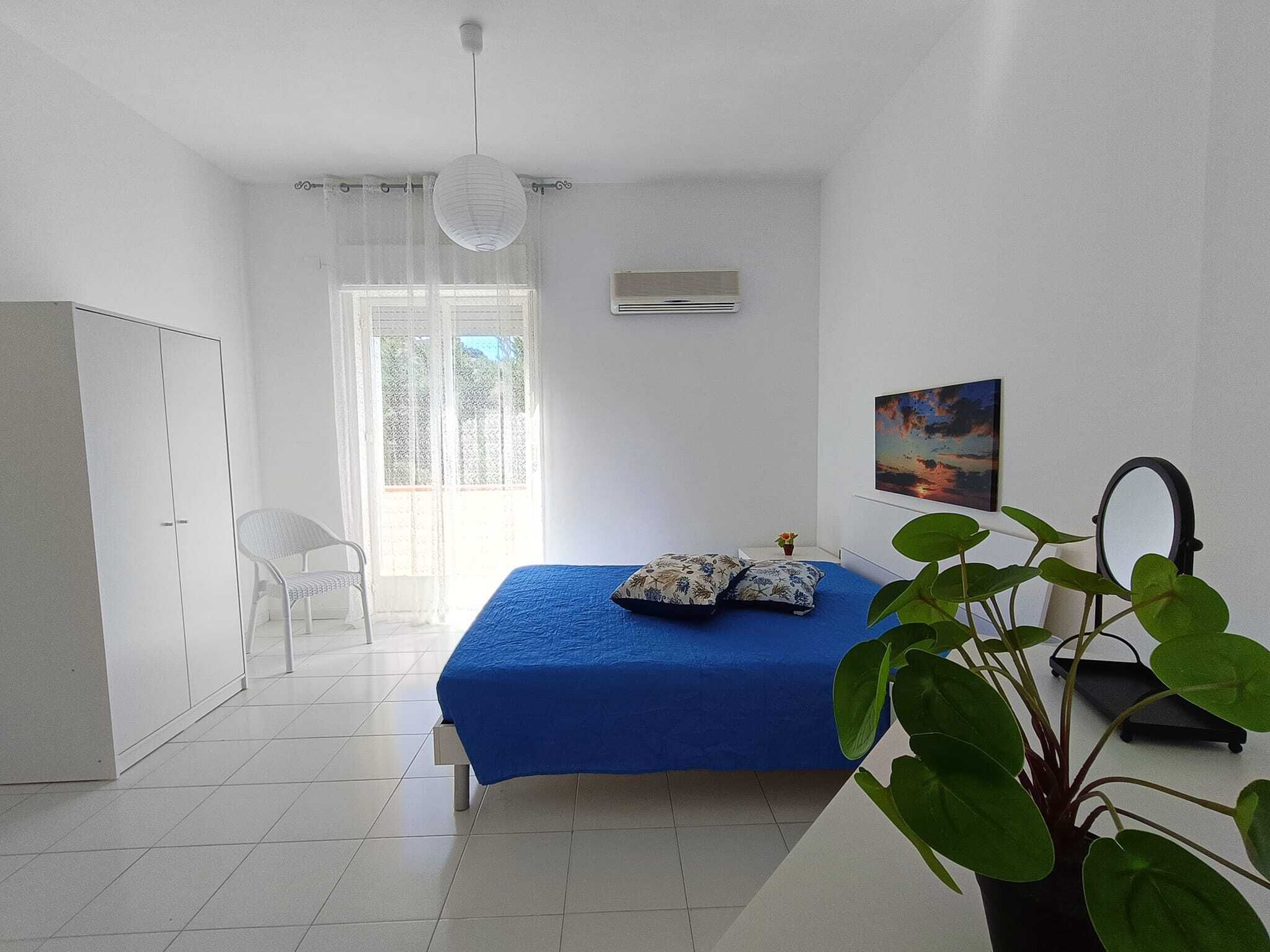 Un dormitorio con cama, una silla, un armario, un ventanal y una planta.