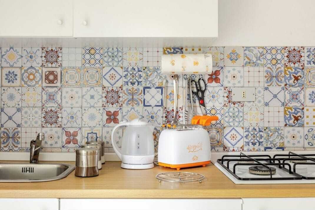 Une cuisine avec un plan de travail recouvert de carreaux, un évier, une bouilloire, un grille-pain et une cuisinière à gaz.