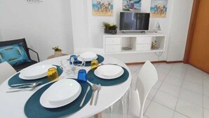 A dining area with a round table set for four, white chairs, and a white cabinet with a TV and decorative items. - Appartamenti Abate Riva del Golfo Home (Alcamo)
