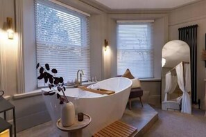 Une salle de bain moderne avec une baignoire sur pieds, un banc en bois et un vase décoratif.