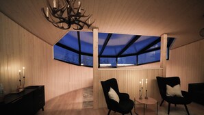 A cozy room with wooden walls, a skylight, a chandelier, and two chairs with a small table. - Livo Arctic (Posio)