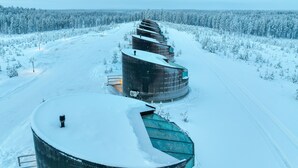 A modern building with a curved roof, surrounded by a snowy landscape and dense forest. - Livo Arctic (Posio)