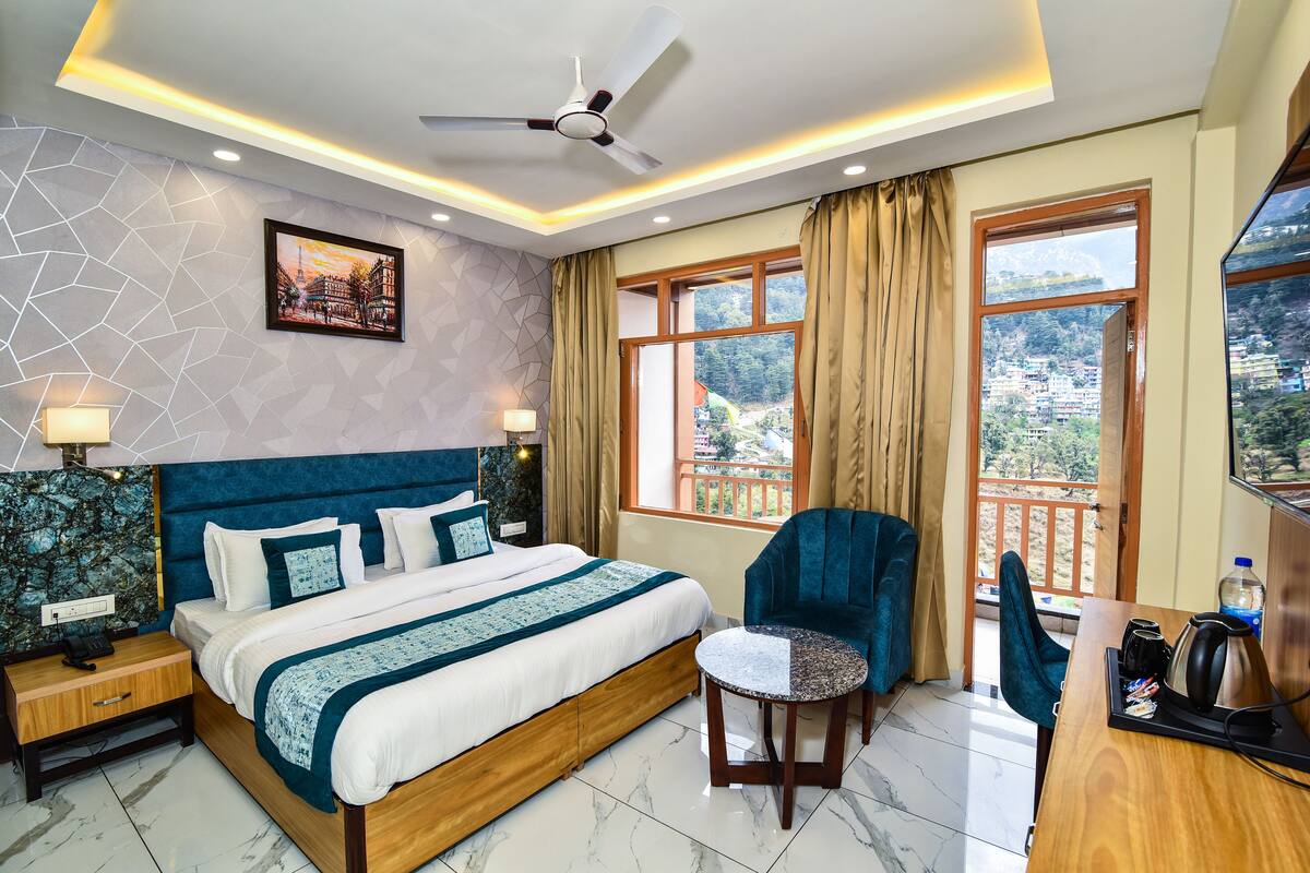 A hotel room with a large bed, a desk with a chair, a ceiling fan, and a window with curtains.