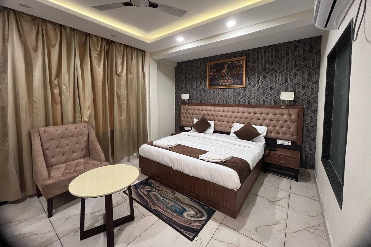 A modern hotel room with a tufted headboard bed, a round table, a sofa, and a ceiling fan.