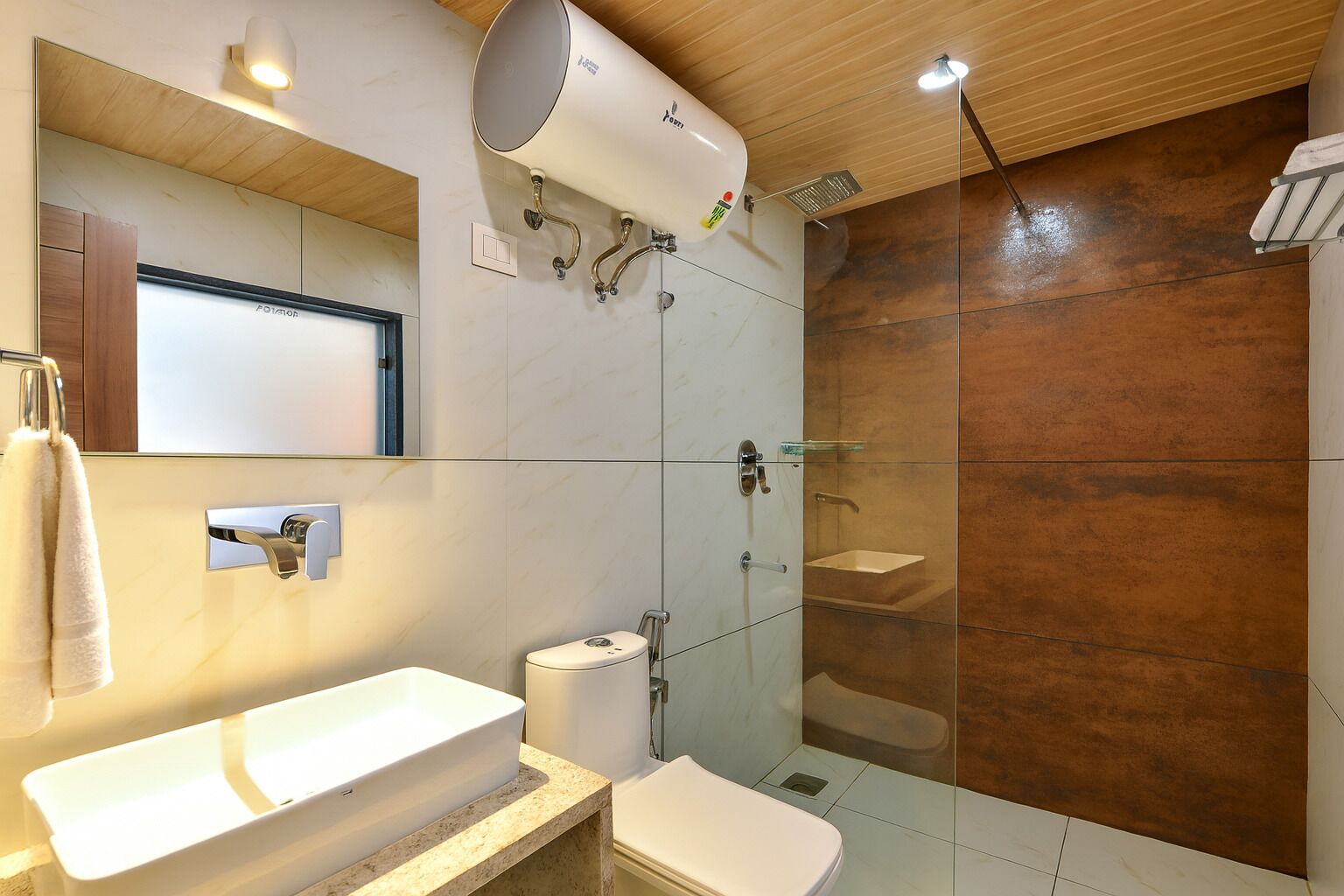 Une salle de bain moderne avec un grand miroir, un lavabo blanc, des toilettes et une douche séparée par une paroi de verre.