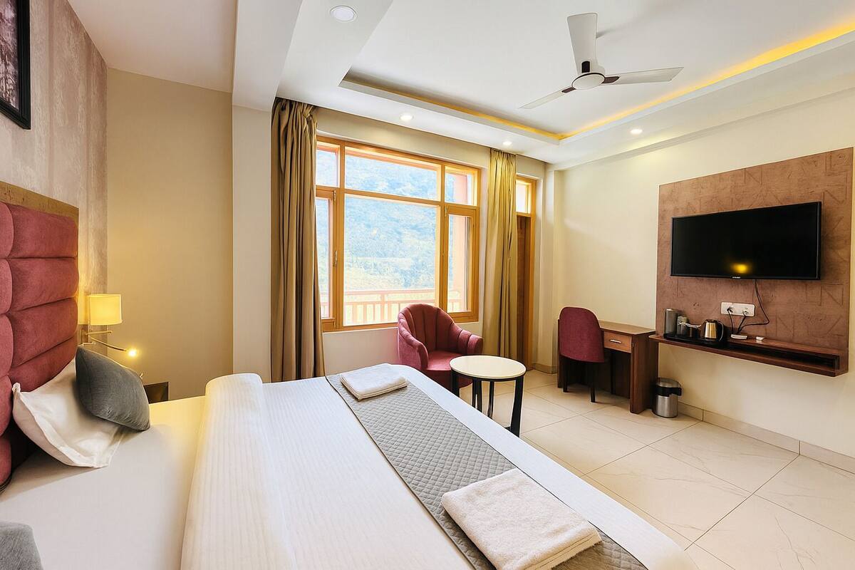 A hotel room with a bed, a desk, a chair, a TV, and a window with curtains.