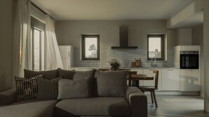 Een moderne woonkamer met een bank, een eettafel en een keukenhoek met witte kasten en een inbouwoven.