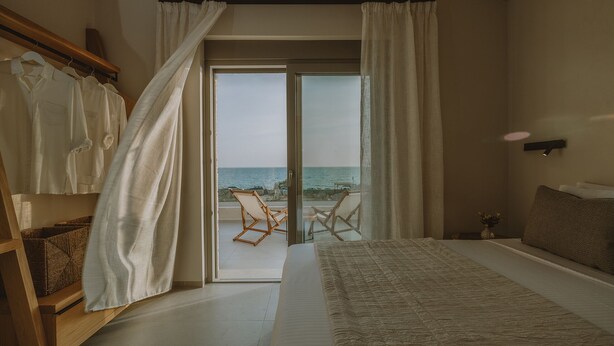 Een slaapkamer met een groot bed, een houten garderobe, een stoel bij het raam en uitzicht op zee.