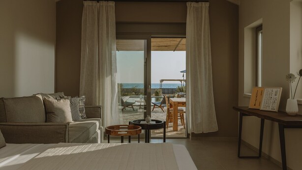 Un dormitorio con una cama grande, un sofá, una mesita y vistas a un patio exterior con una mesa y sillas.