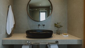 Un baño moderno con un espejo redondo, un lavabo tipo recipiente negro y dos toallas colgadas en un perchero.