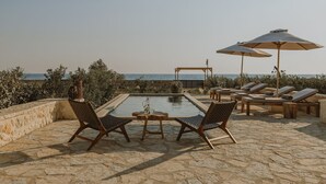 Zona junto a la piscina con mesa y sillas, sillones reclinables y sombrillas.