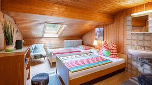 A cozy, wooden-paneled room with two beds, a small desk, and a bathroom with a sink and mirror. - Ferienwohnung Bergblick (Oberaudorf)