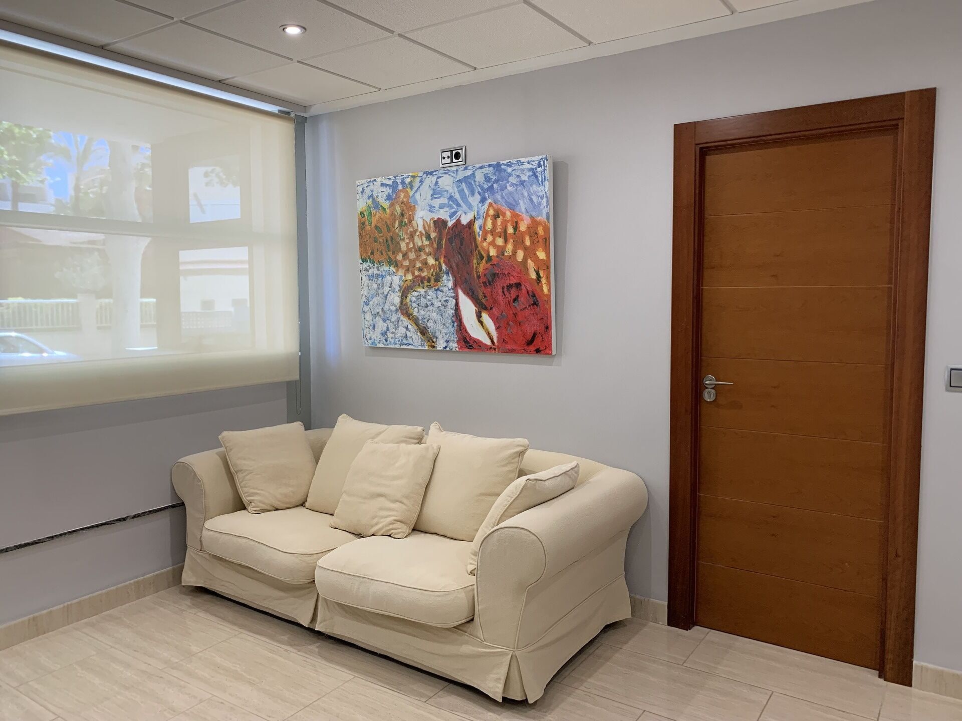 A room with a beige sofa, a wooden door, and a colorful abstract painting on the wall.