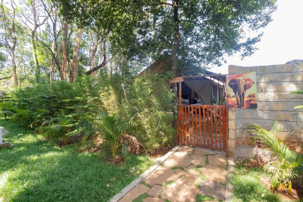Une entrée de jardin agrémentée d’un portail en bois, d’un chemin de pierres et d’une fresque représentant un éléphant sur un mur de pierre.