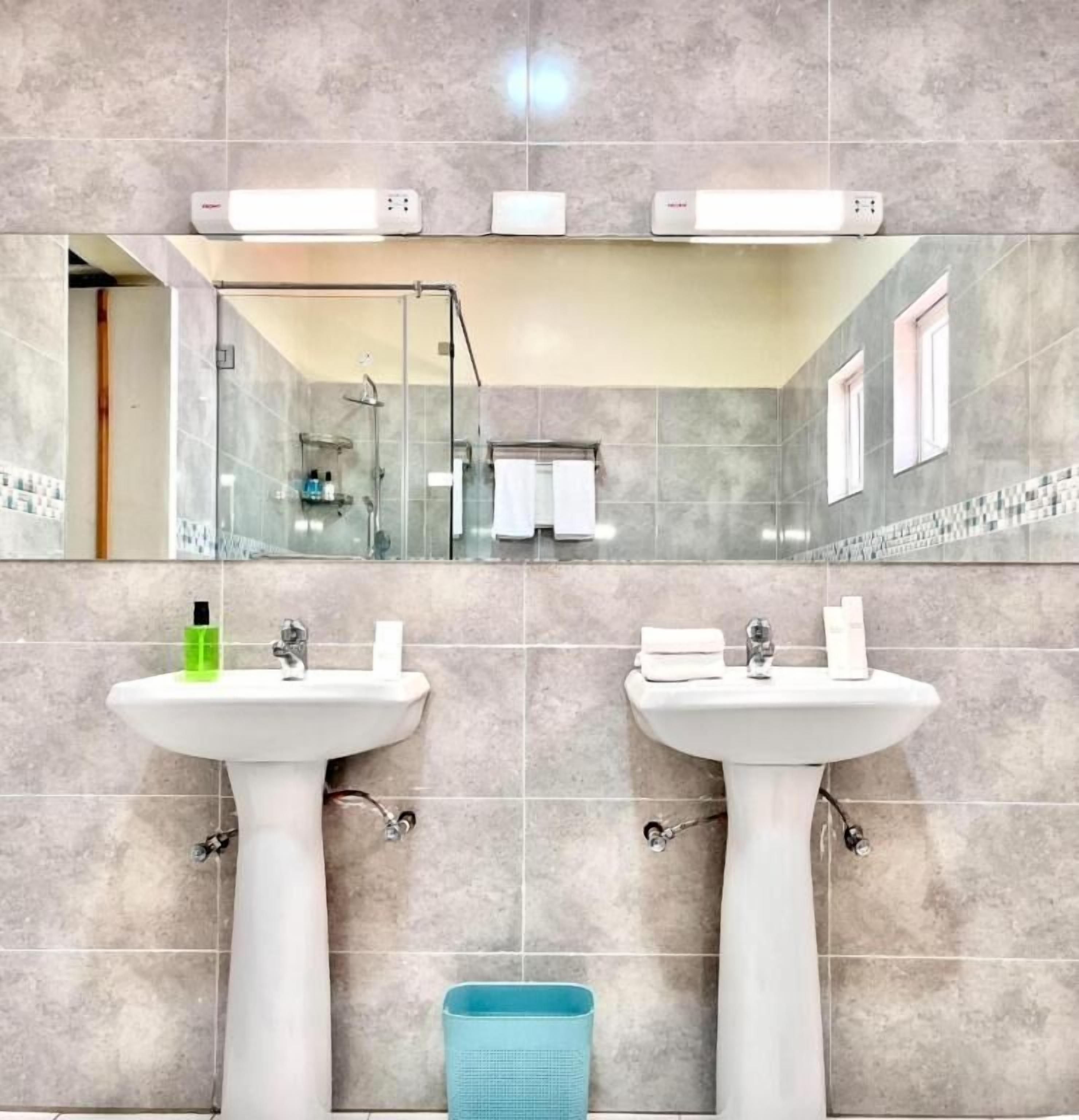 A bathroom with two sinks, a glass shower enclosure, and a blue trash bin.