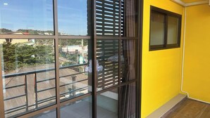 A room with a large window, a yellow wall, and a visible balcony. - J & Ariya Hotel (Koh Samui)