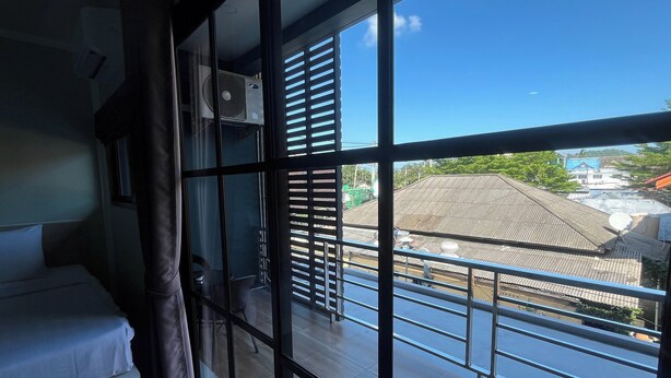 A room with a large window, a bed, a chair, and a curtain. - J & Ariya Hotel (Koh Samui)