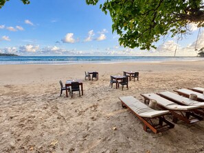 Un área de comedor frente a la playa, con mesas y sillas, con vista al océano.