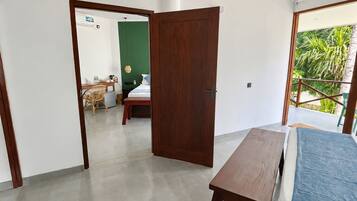 Una stanza con un letto, un tavolo di legno, un ventilatore a soffitto e vista su un balcone con piante.