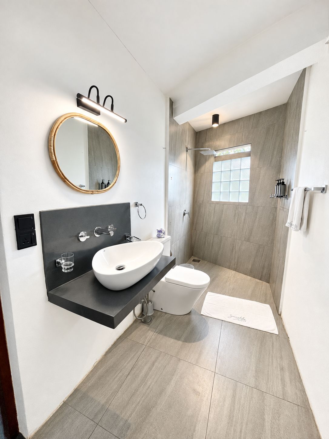 A modern bathroom with a large oval sink, a round mirror, a toilet, and a shower area.